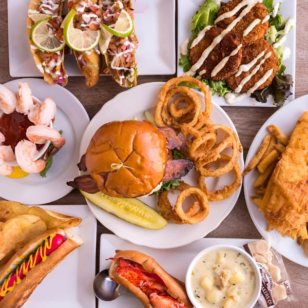 A top-down view of various pub dishes, including tacos, fish and chips, a hot dog, and a lobster roll.