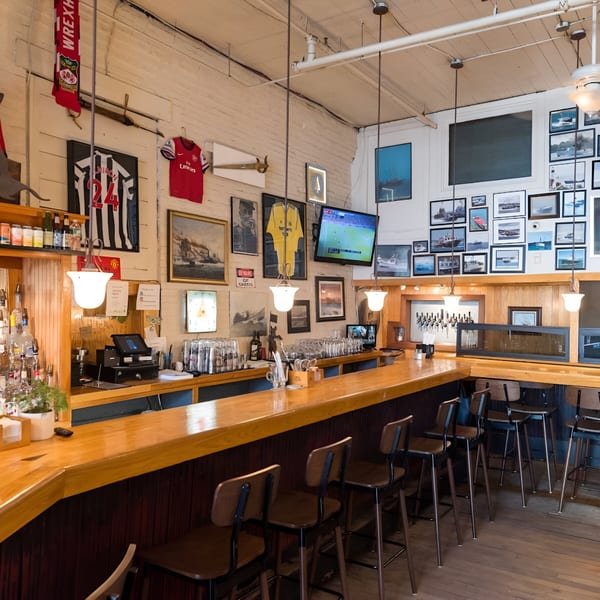 A long wooden bar with stools, decorated with sports jerseys and nautical-themed pictures.