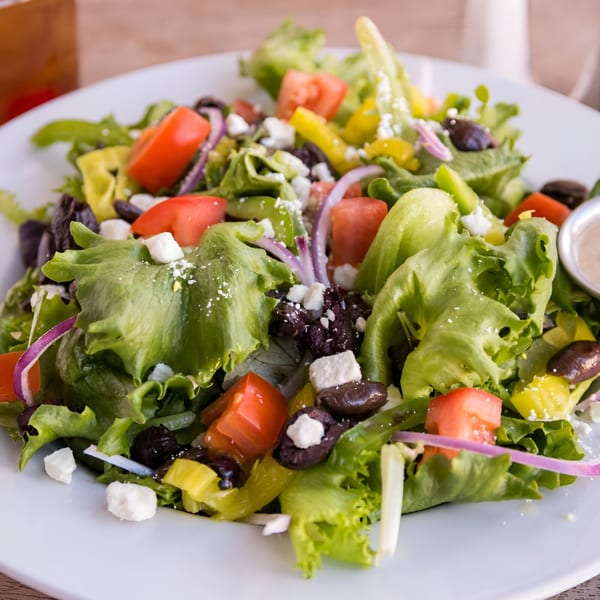 Fresh green salad with tomatoes, black olives, red onion, feta cheese, and peppers.