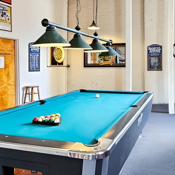 A pool table with racked balls and a cue ball under green hanging lamps at Andy's Old Port Pub.