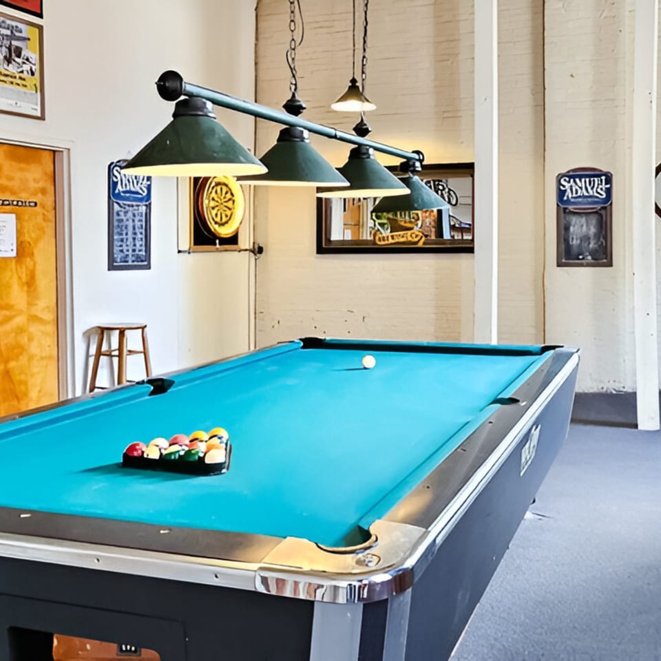 A pool table with racked balls and a cue ball under green hanging lamps at Andy's Old Port Pub.