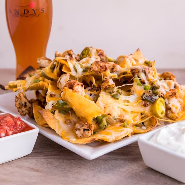A plate of Andy's Old Port Pub nachos with chicken, cheese, jalapeños, salsa, and sour cream.