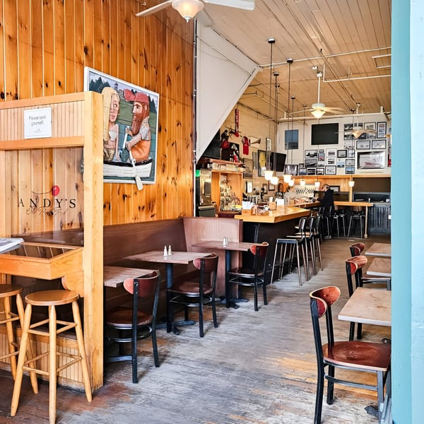 Interior of Andy's Old Port Pub, featuring wooden walls, tables, chairs, and a bar area.