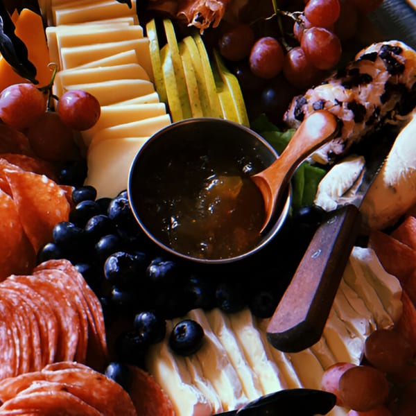 Close-up of a charcuterie board with cheeses, salami, blueberries, grapes, and jam.